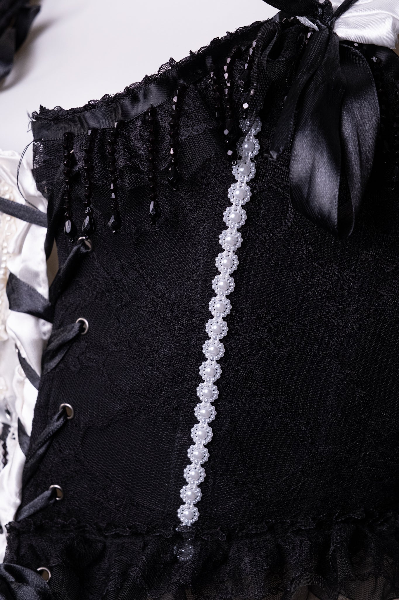 Détail du corset Pierrot noir avec laçage et rangée de dentelle avec  perles blanches