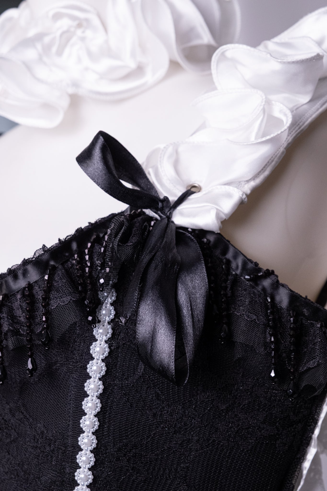 Gros plan du corset Pierrot avec collerette blanche et nœud noir et détail de perles 
